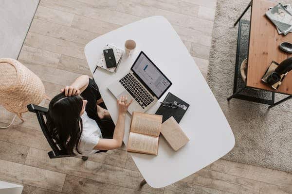 Person working at white table with laptop, books, and coffee cup, overhead view